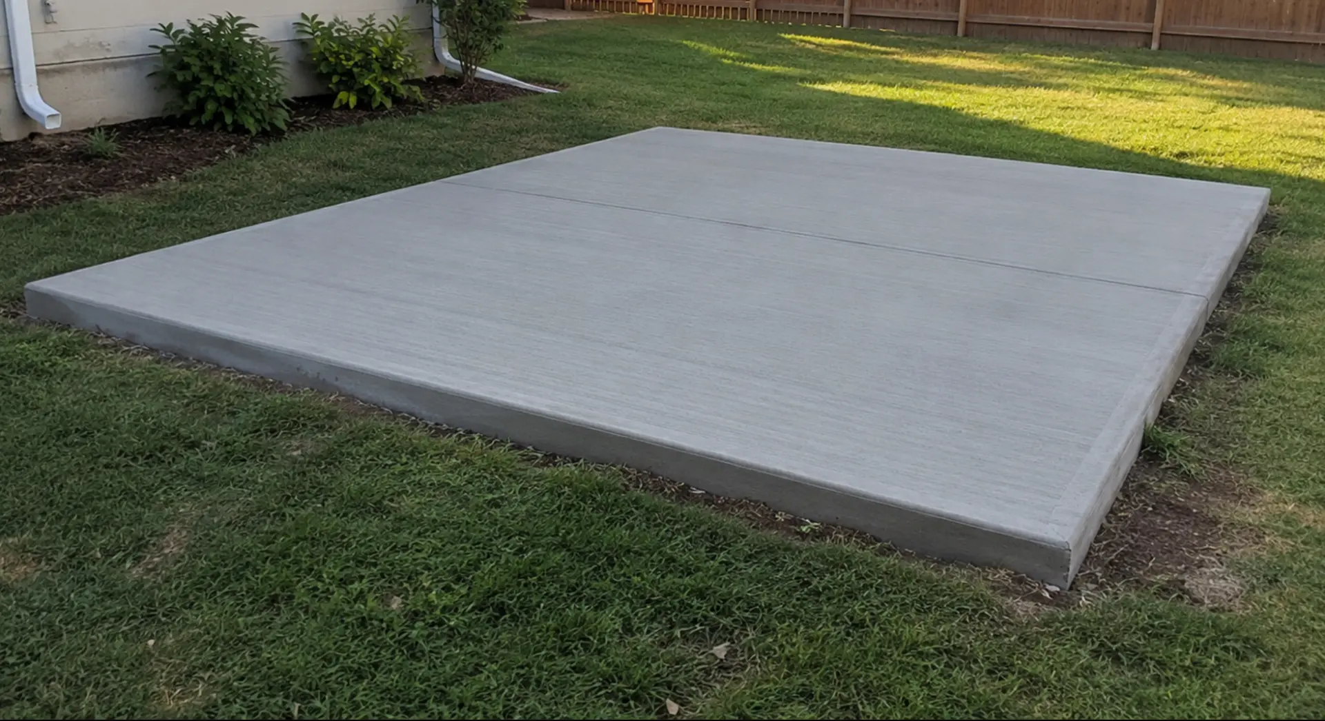 Freshly finished concrete pad beside a residential garage